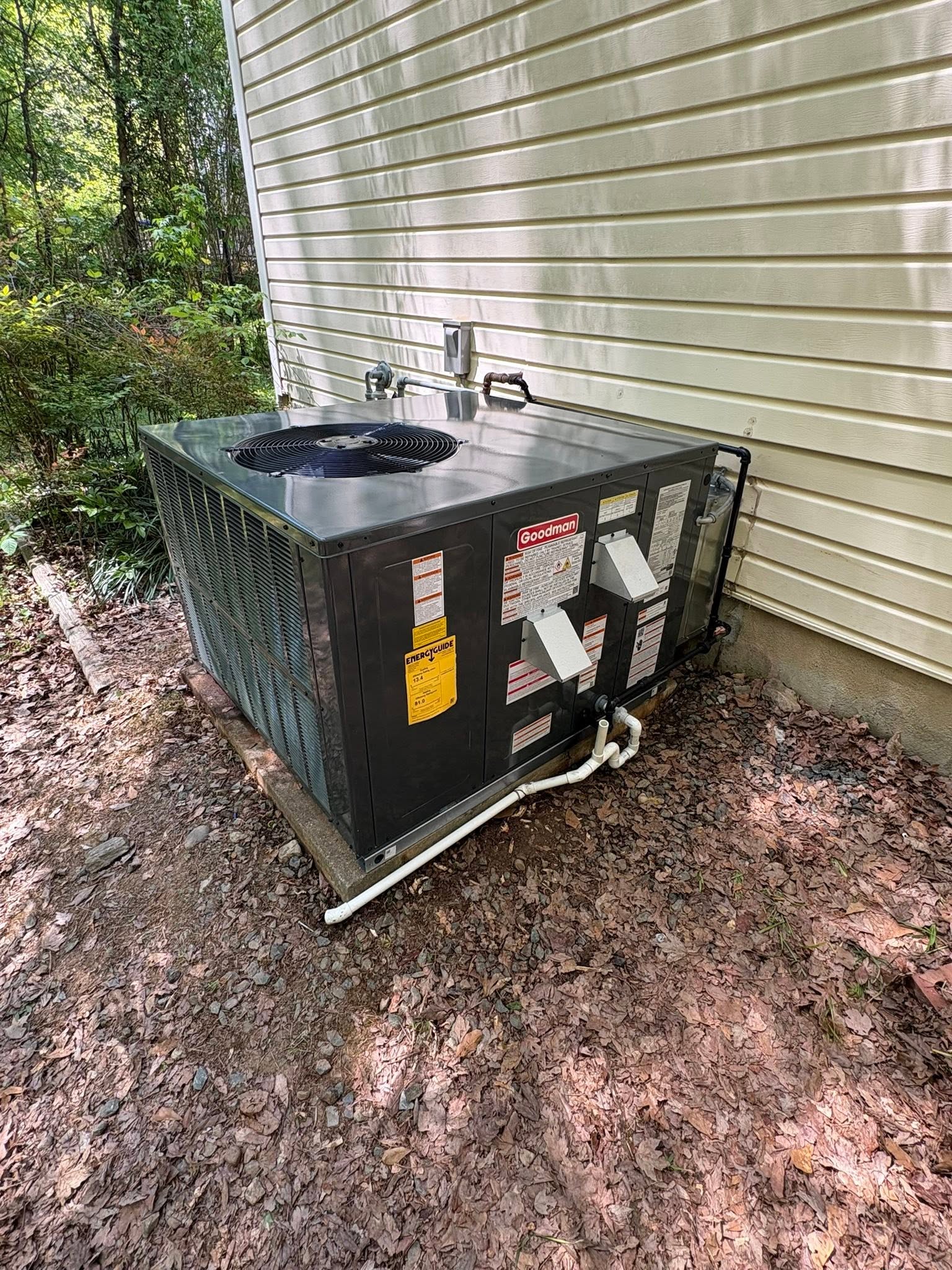 A packaged heating and cooling unit installed beside a home on a wooded lot in the Triangle.